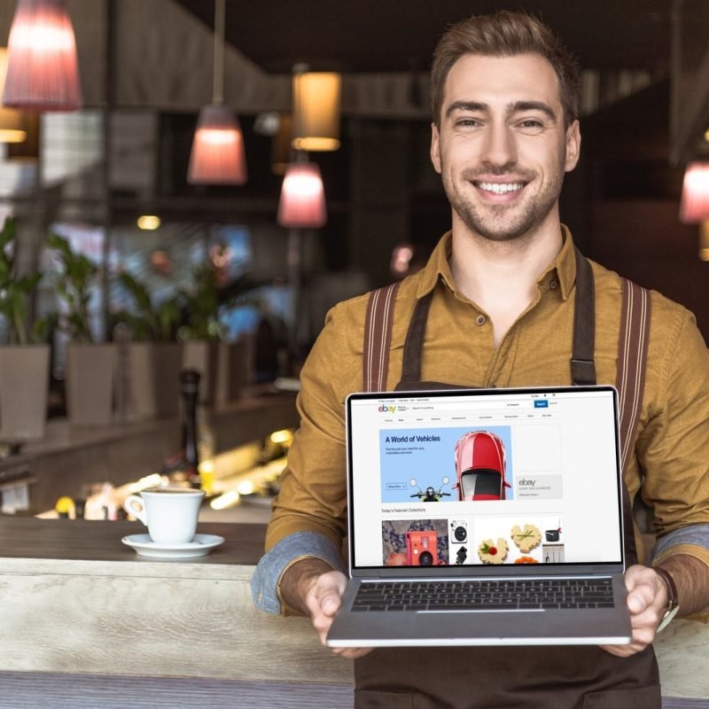smiling-young-waiter-holding-laptop-with-ebay-website-on-screen-in-cafe.jpg